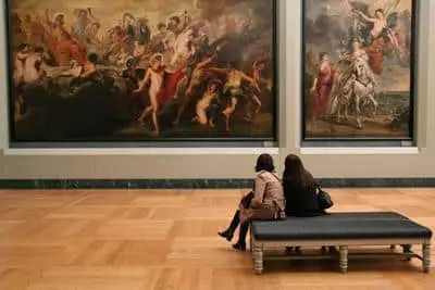 Two women take in an old painting Inside the Louvre museum in Paris.