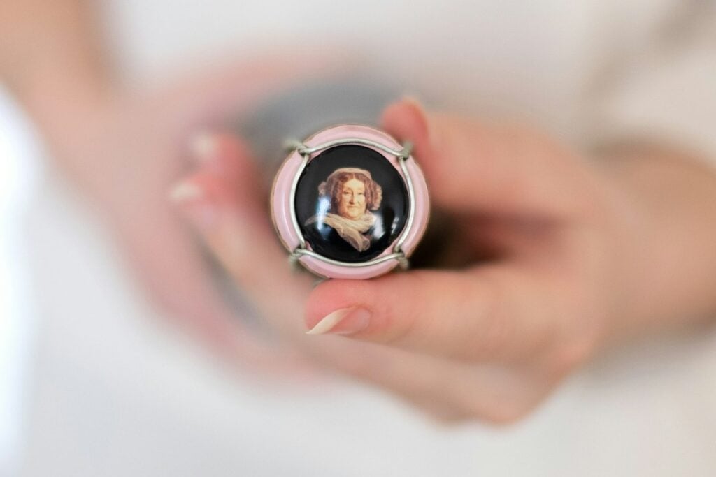 Hands holding a Veuve Clicquot champagne cap bearing the portrait of Madame Clicquot