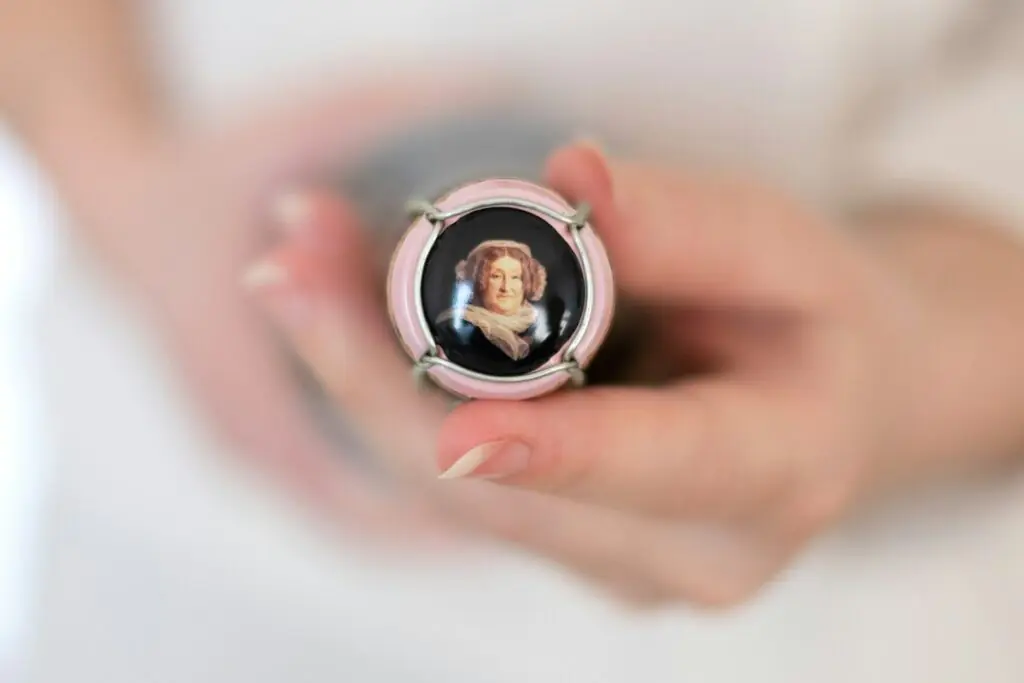 Hands holding a Veuve Clicquot champagne cap bearing the portrait of Madame Clicquot